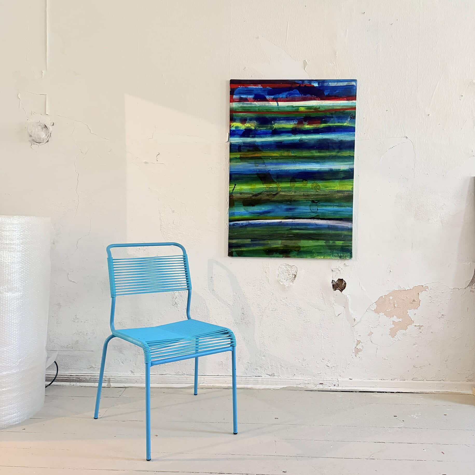 Farbenfrohes abstraktes Gemälde mit horizontalen Linien in Blau, Grün und Rot, an einer weißen Wand in einem Atelier.