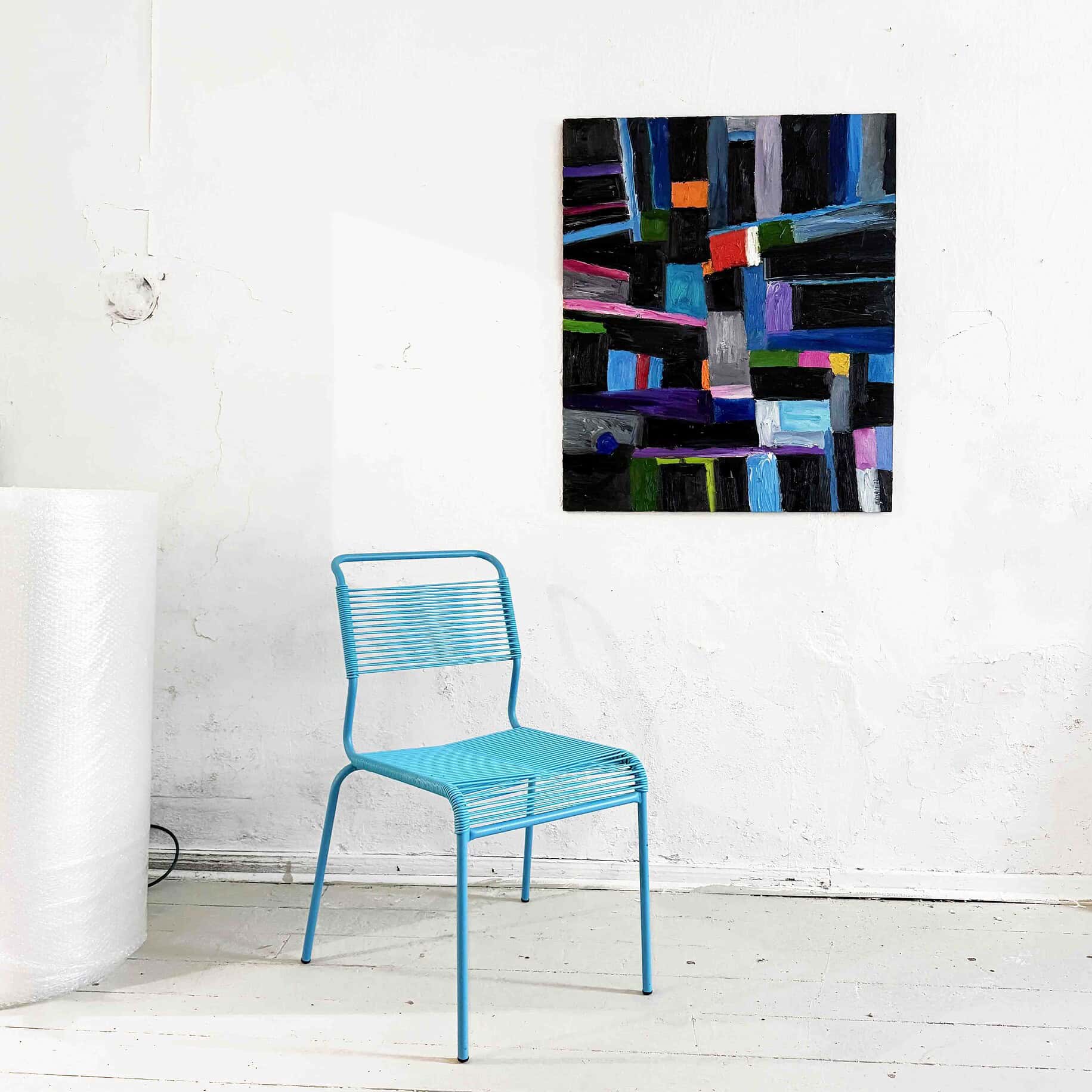 Farbenfrohes abstraktes Gemälde an weißer Wand mit blauer Metallstuhl im Vordergrund, typische Kunst- und Design-Atmosphäre.