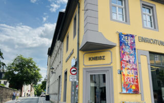 Farbenfrohes Wandbild an der gelben Fassade des Knesiz-Ateliers für Malerei und Auftragsmalerei in Dresden.