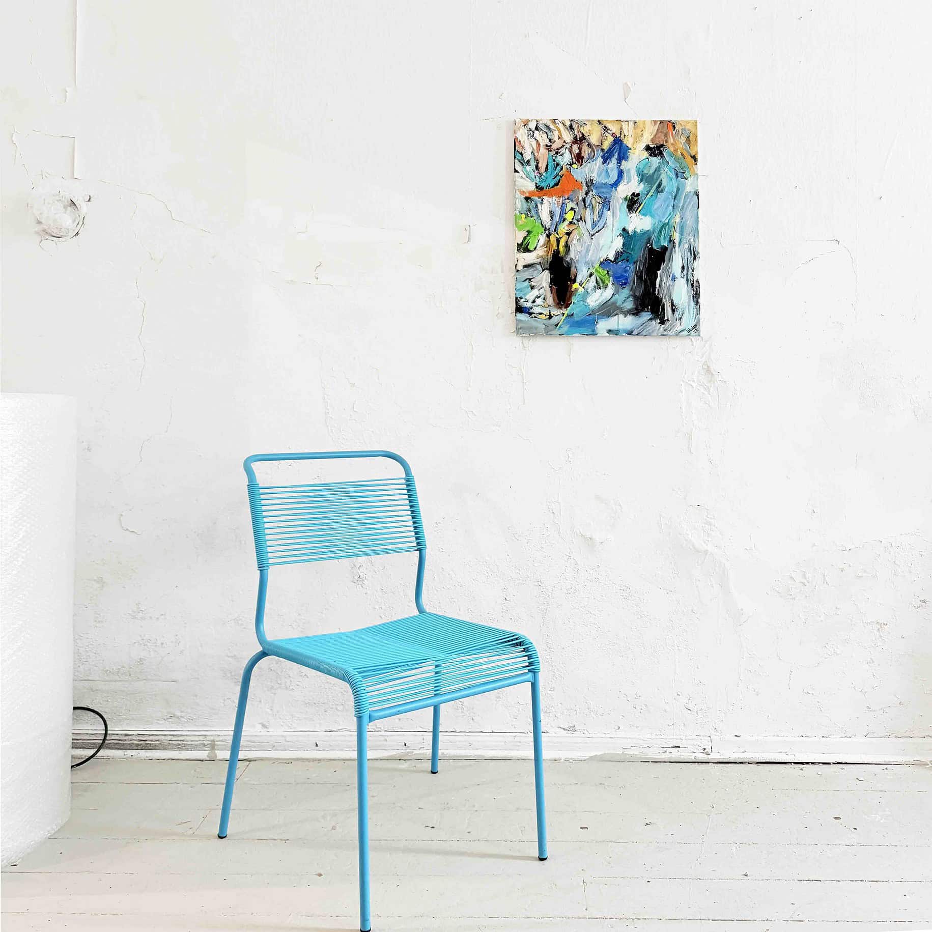 Blaue Metallstuhl im Galerieambiente mit abstrakter Malerei an weißer Wand.