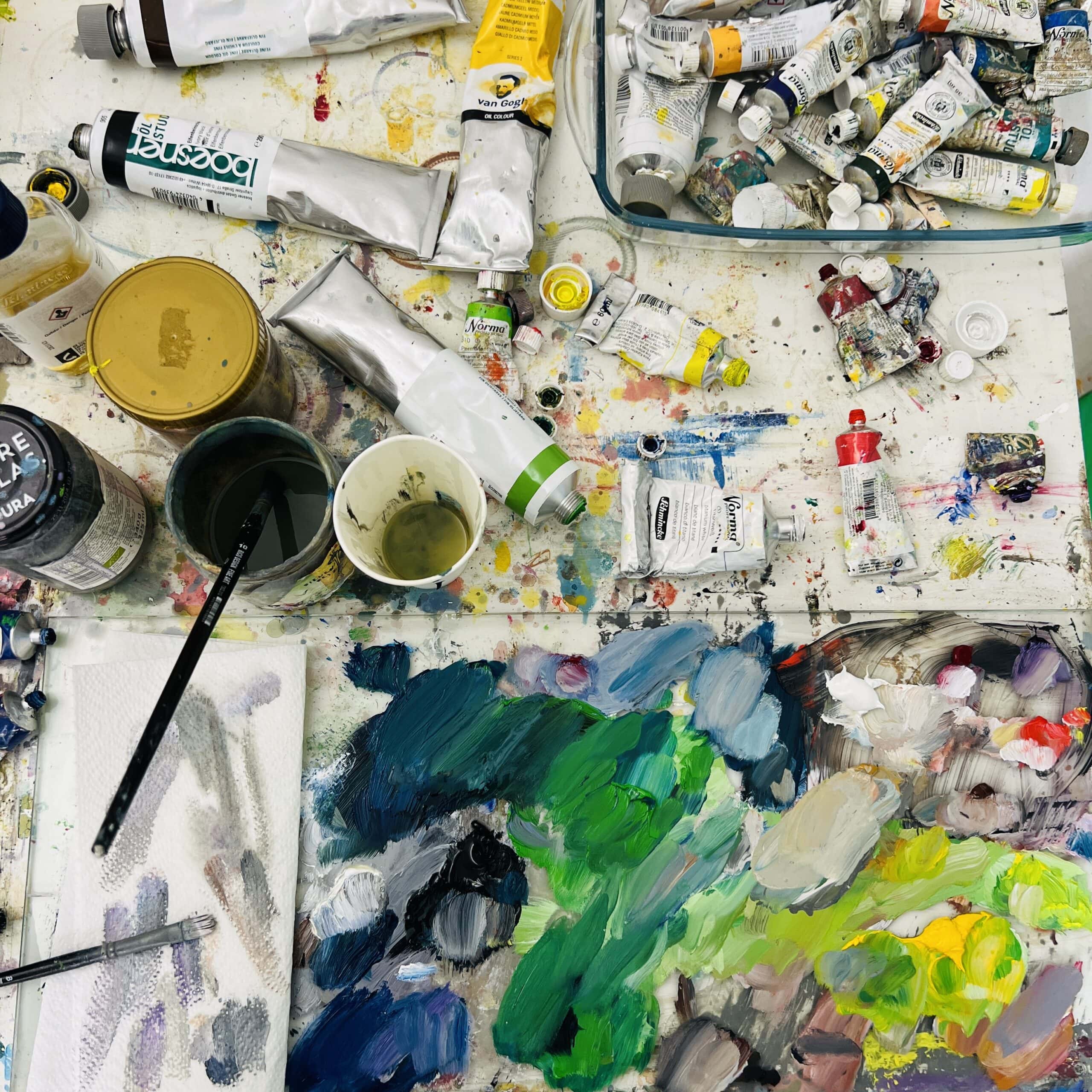 kunstkopie malen lassen im atelier nikolaus kriese deutschland Farben und Malutensilien auf einem Künstlerarbeitsplatz, Fokus auf kreative Malerei, Ölfarben, Acryl und Pinsel, ideal für Auftragsmalerei und künstlerische Werke.