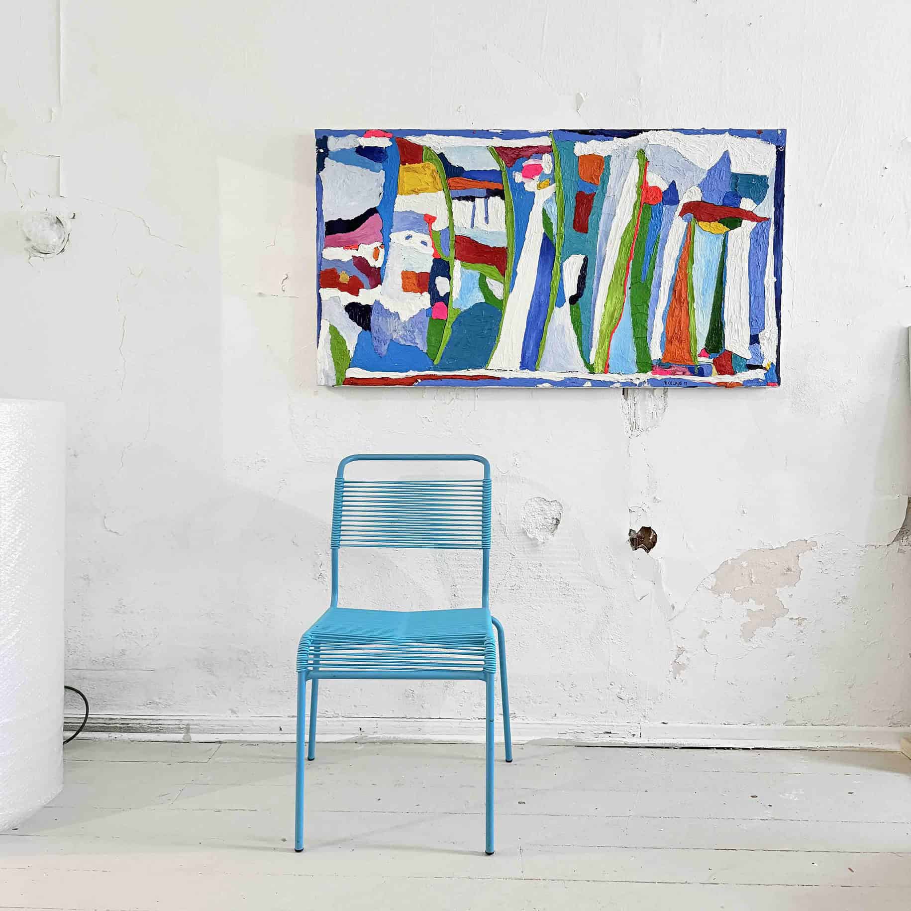 Lebendige abstrakte Malerei mit bunten Formen und Linien, hängt an einer weißen Wand in einem Kunststudio ebenso like einer blauen Metall-Stuhl.