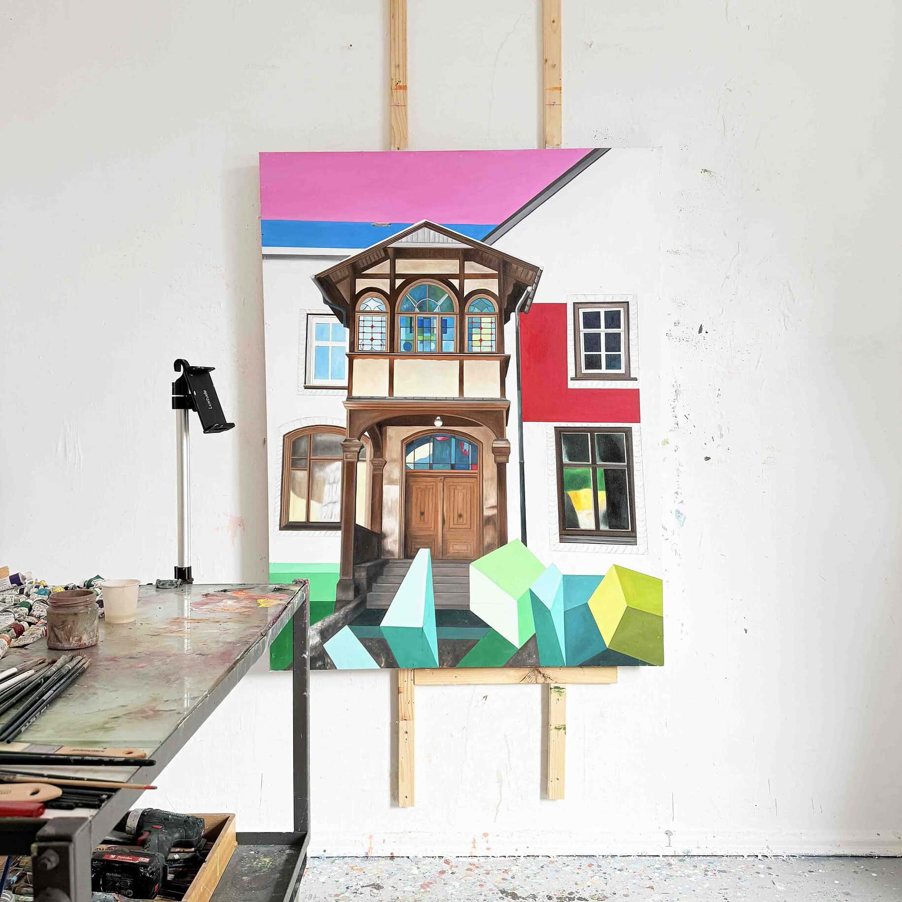 Farbenfrohes Gemälde eines mit Türen und Fenstern gestalteten Hauses, das auf einer weißen Wand im Atelier hängt.