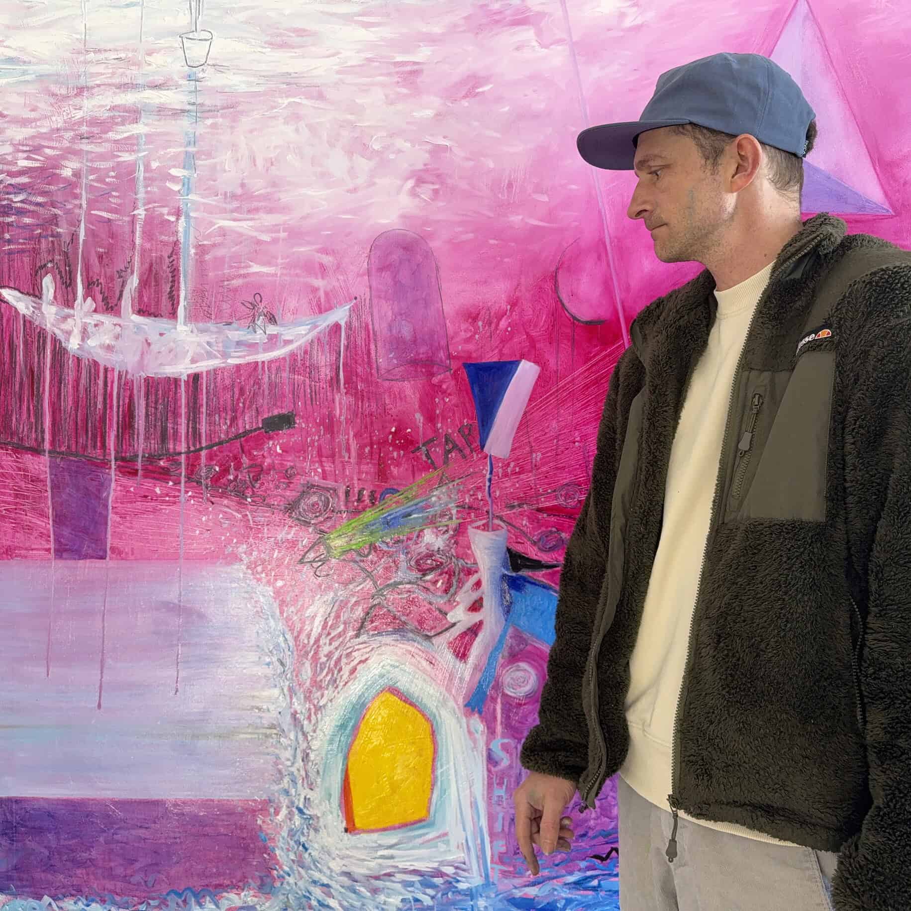 Künstler Nikolaus Kriese betrachtet sein abstraktes Gemälde mit pinken und blauen Farbtönen, das im Hintergrund eine kreative und lebendige Atmosphäre schafft.