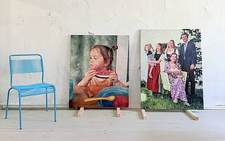 Innenraum mit zwei realistischen Familienporträts auf Leinwand, einem kleinen blauen Metallstuhl, rustikalen weißen Boden und Wand, ideal für maßgeschneiderte Malerei- und Auftragskunst.
