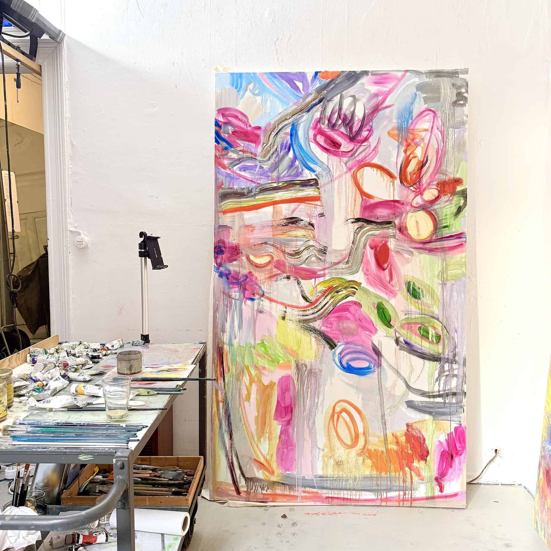 Künstleratelier mit großen abstrakten Gemälden, Farbtuben und Pinseln auf einem Tisch, kreative Arbeitsumgebung, Inspiriertes Kunstwerk in Entstehung, zeitgenössische Kunst, Inspiration und Farben.